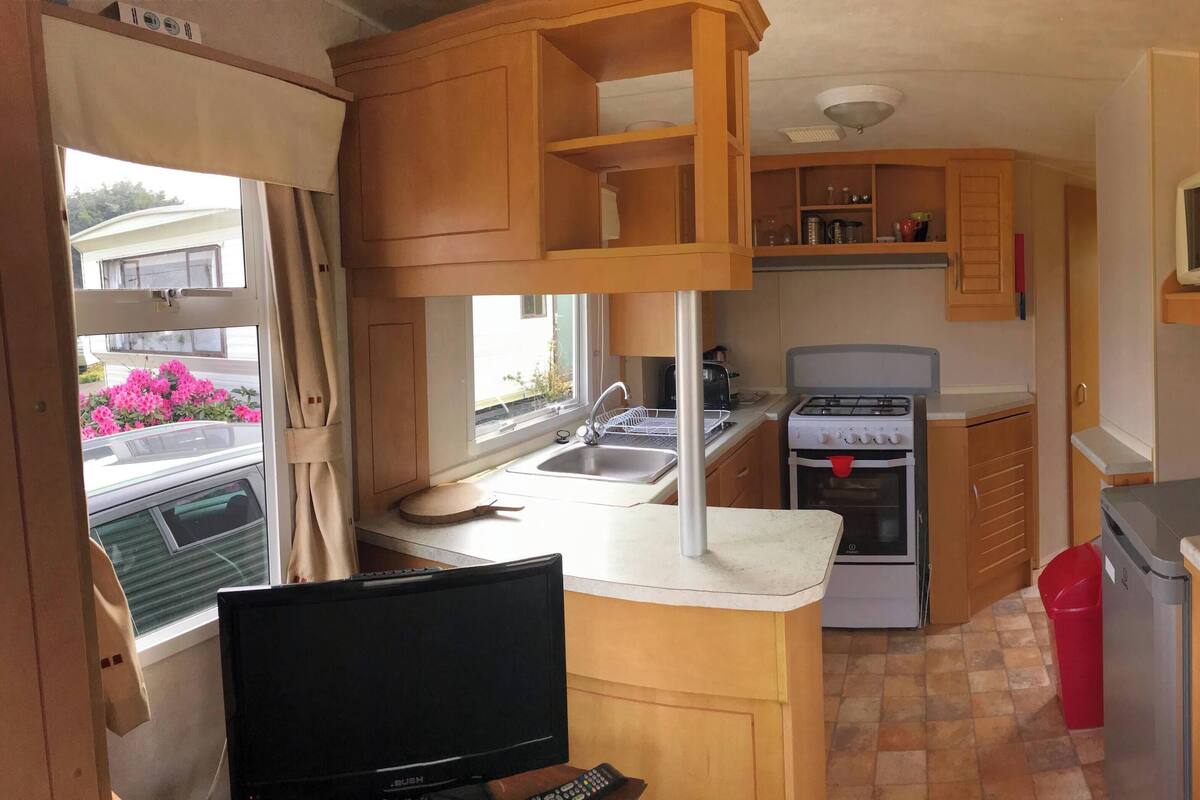 A compact kitchen with a stove, microwave, sink, and a television.