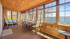 Una habitación con paneles de madera, una ventana grande con vistas a un cuerpo de agua, una mesa de comedor con sillas y un banco con cojines.