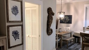 Un couloir orné de tableaux encadrés, une porte fermée, un coin repas avec une table et des chaises, et un luminaire suspendu.