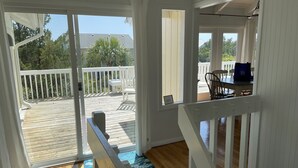 Une pièce dotée d’un plancher en bois, d’une rambarde blanche et offrant une vue sur une terrasse aménagée avec du mobilier d’extérieur.