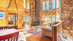 Un acogedor interior de cabaña con paredes de madera, una chimenea, un comedor y una sala de estar con sofá y mesa de centro.