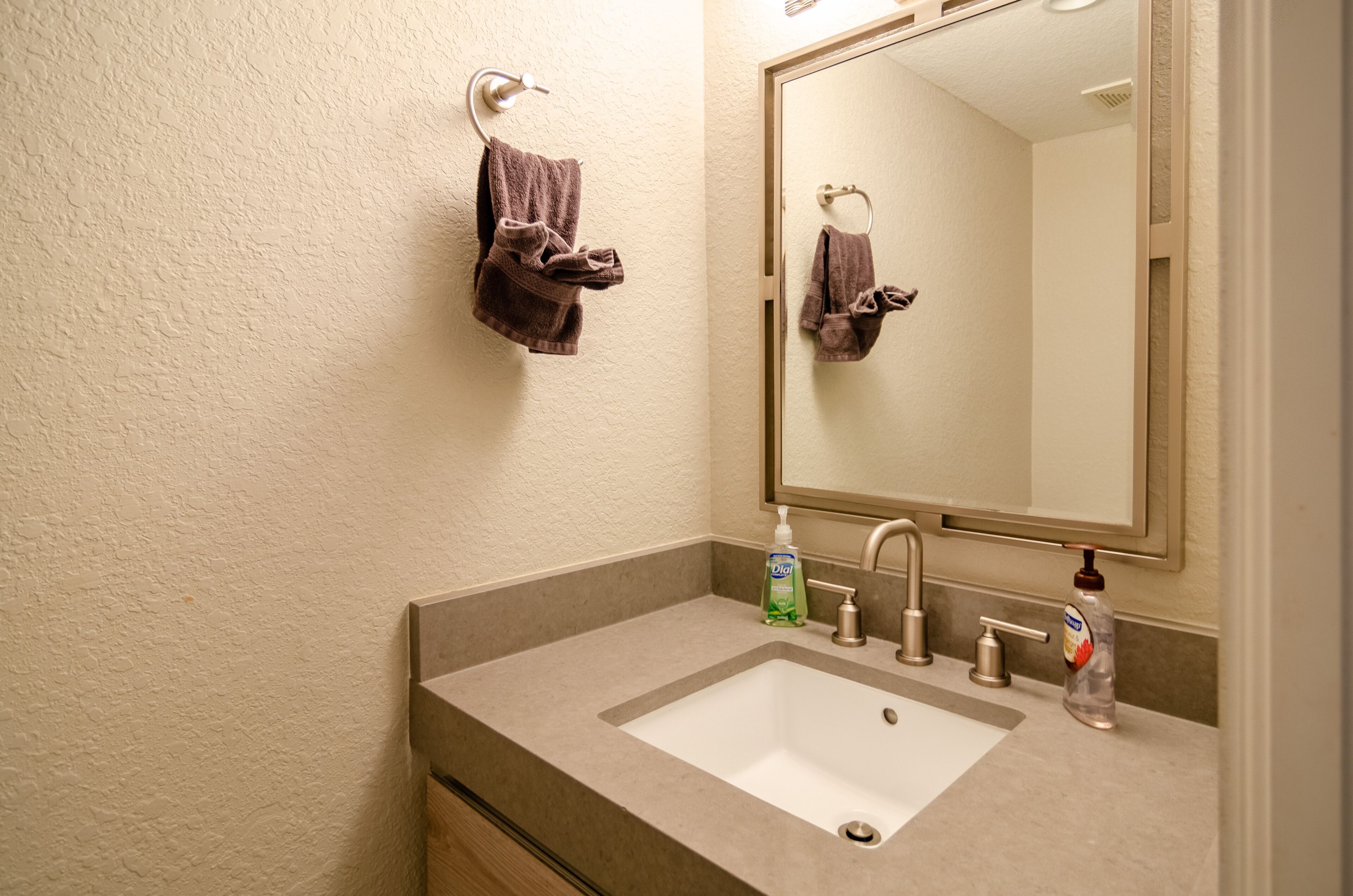 Un baño con un lavamanos blanco, un espejo y dos toallas colgadas de ganchos.