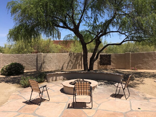 An outdoor patio with stone flooring, a fire pit, and two chairs.