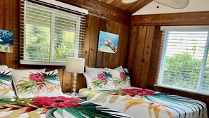 A room with wooden walls and ceiling, two beds with floral bedspreads, a ceiling fan, and windows with blinds. - BEACHFRONT MAUI KIHEI HOUSE (Kihei)