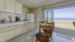 Une cuisine avec vue sur la plage, un coin repas avec une table et des chaises, et un réfrigérateur.