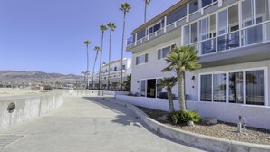 Un immeuble moderne à plusieurs étages, doté de grandes fenêtres et d’un balcon, entouré de palmiers et surplombant un ciel dégagé.