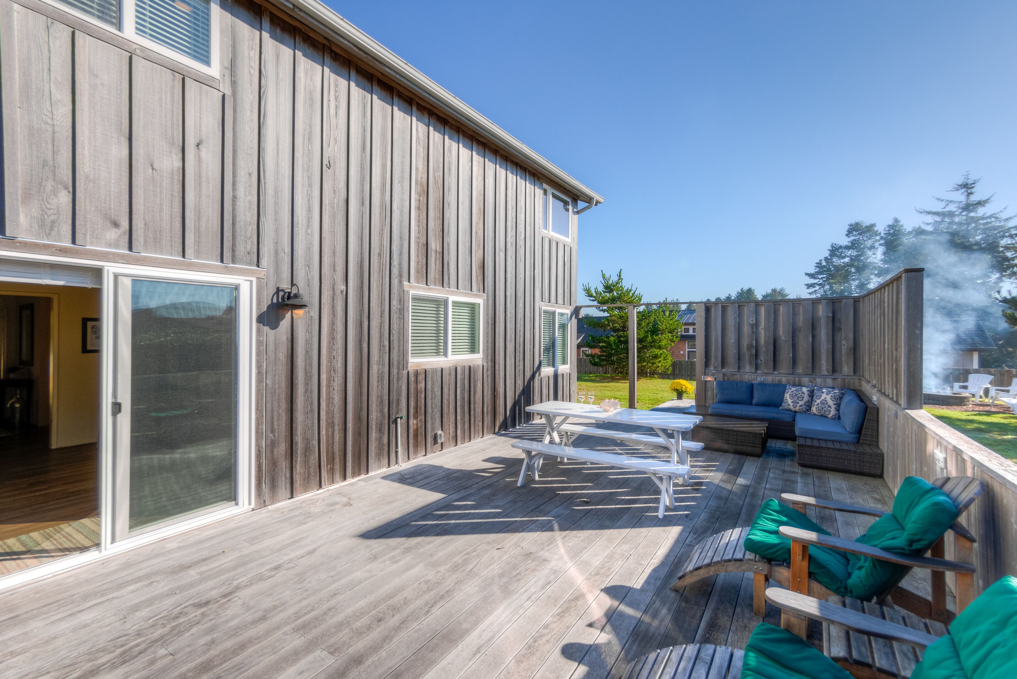En træterrasse med udendørs møbler, en skydedør og et overdækket siddeområde.