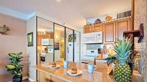 A kitchen with wooden cabinets, a granite countertop, and a microwave. There are two chairs and a potted plant.