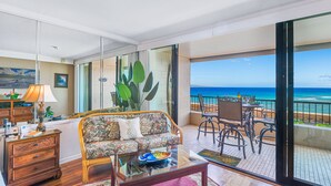 A spacious living area with a sofa, coffee table, and a balcony with a view of the ocean.