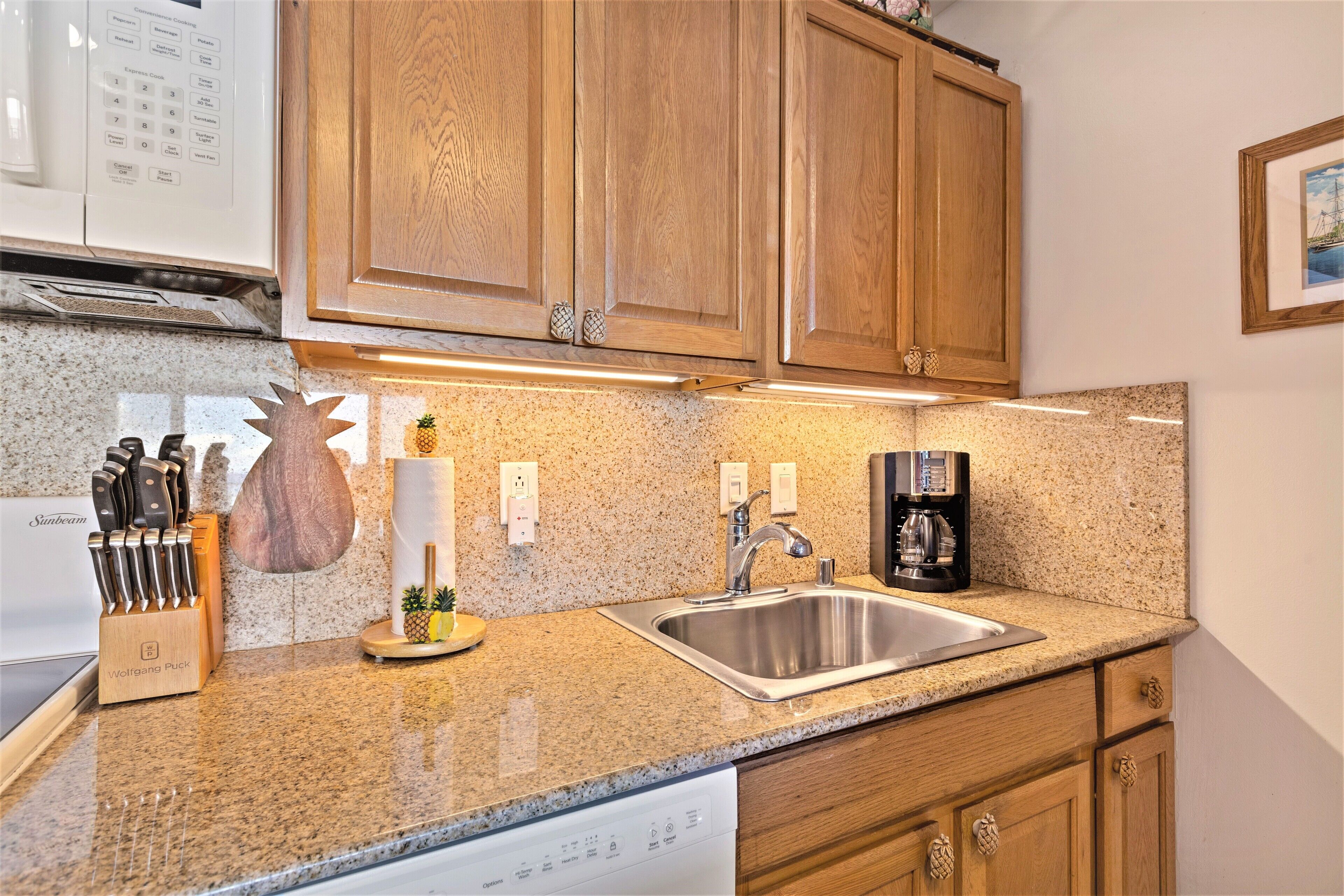A kitchen with granite countertops, wooden cabinets, a stainless steel sink, and a coffee maker.
