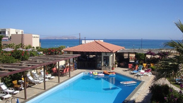 Area piscina con lettini, un piccolo edificio con tetto in tegole rosse e vista sul mare.
