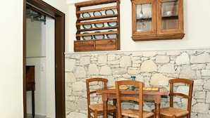 Zona pranzo con parete in pietra, sedie di legno, tavolo di legno e un mobile con ante in vetro.