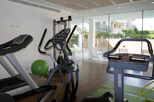 Un gimnasio con máquinas de cardio, una pelota de ejercicio verde y vistas a un balcón con mobiliario exterior.