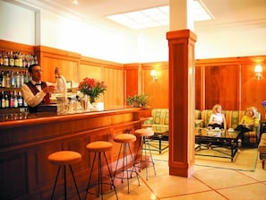 A bar area with stools, a bartender, and a seating area with sofas and a table.