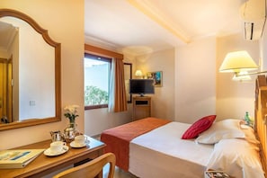 A hotel room with a bed, a desk with a chair, a television, and a window with curtains.