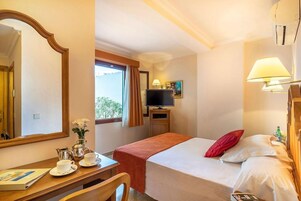 Una habitación de hotel con cama, escritorio con silla, televisor y ventana con cortinas.