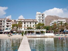 Un hotel frente al mar con un muelle largo, asientos en la playa y varios balcones.