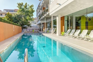 A swimming pool with lounge chairs and umbrellas, surrounded by a wooden fence and glass walls. - Miramar (Pollensa)