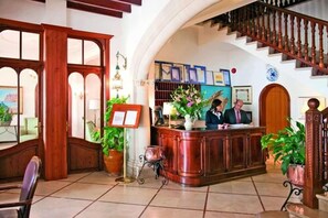 A reception area with a wooden desk, a staircase, and potted plants.