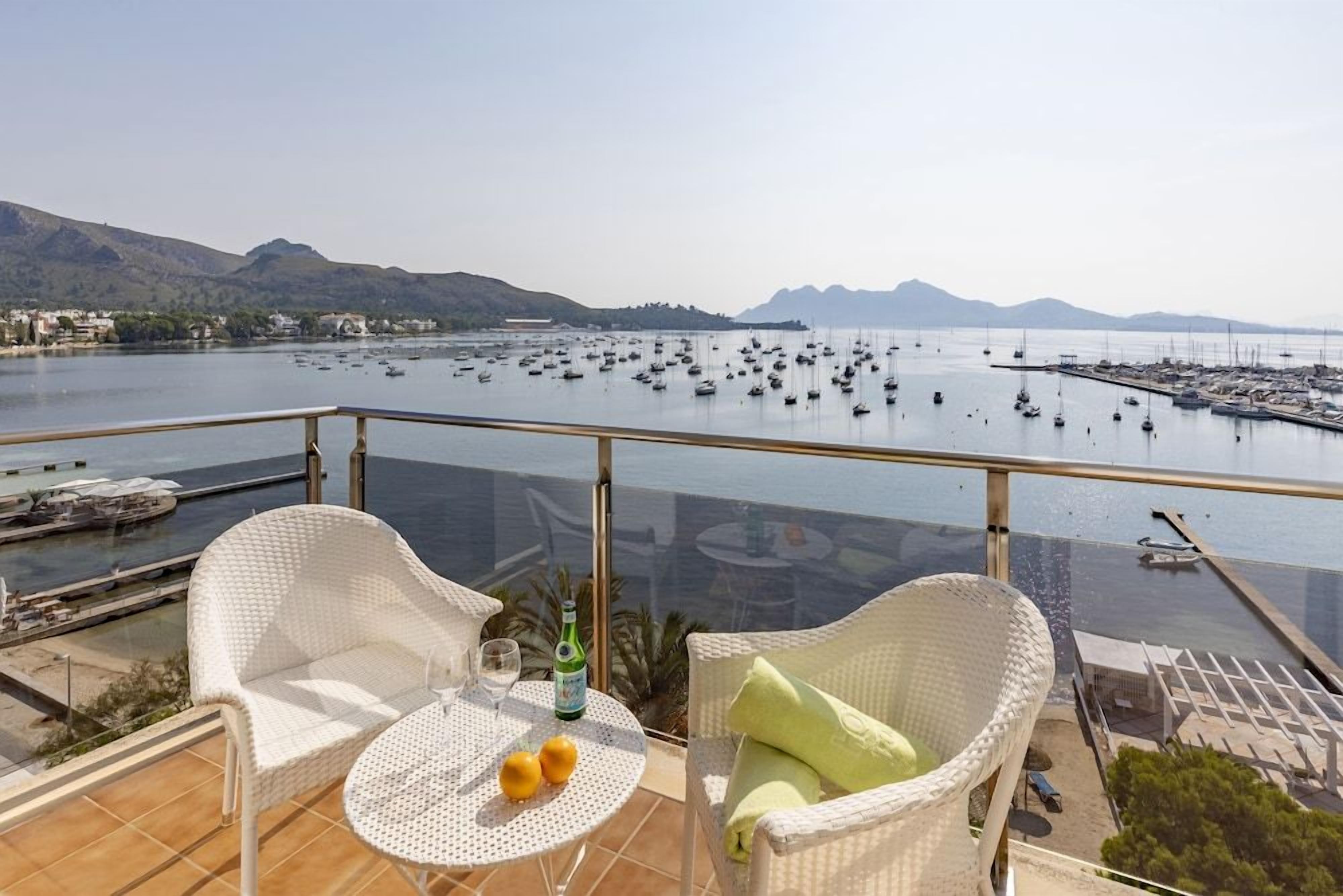 A balcony with wicker furniture, a table with drinks, and a view of a marina with boats.