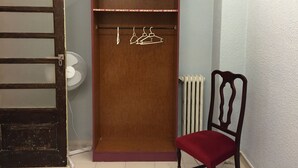 Una habitación con un armario de madera, un radiador, una silla y un ventilador.