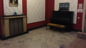 Una habitación con un piano, un banco, una chimenea y un cuadro en la pared.