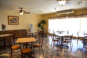 Un comedor de hotel con varias mesas y sillas, ventiladores de techo y un equipo de aire acondicionado.