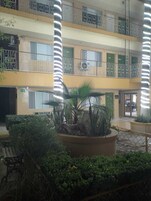 Un edificio de varios niveles con balcones, un patio central con plantas y una fuente de agua.