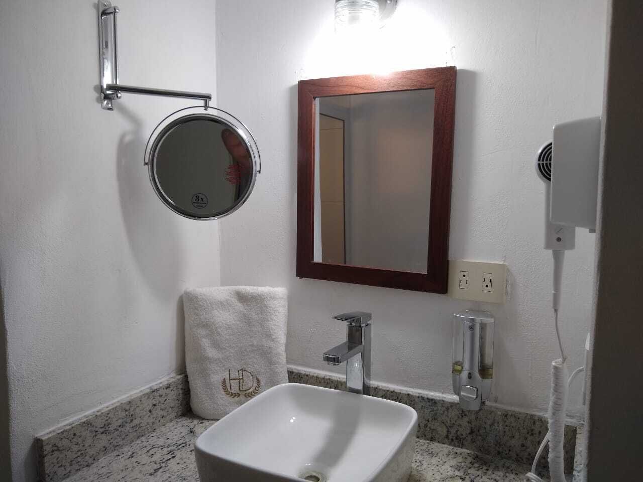 A bathroom with a white sink, a round mirror, and a towel with a logo.