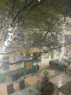 An outdoor seating area with tables and chairs, surrounded by greenery and a building with a green sign. - Hotel el Dorado (Sabinas)