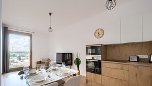 Una cocina moderna con armarios de madera, un comedor con una mesa dispuesta para cuatro personas, un televisor y un reloj en la pared.