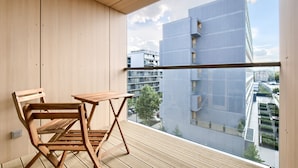 Un balcón con mesa y sillas de madera, vista a un edificio moderno y cielo despejado.