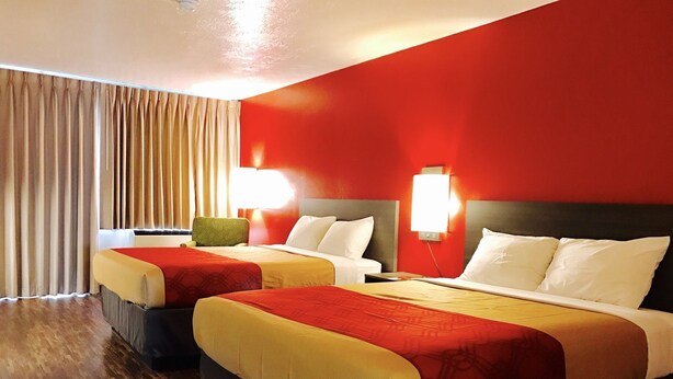 A hotel room with two beds, a large window with curtains, and a red wall. - Econo Lodge Idaho Falls (Idaho Falls)