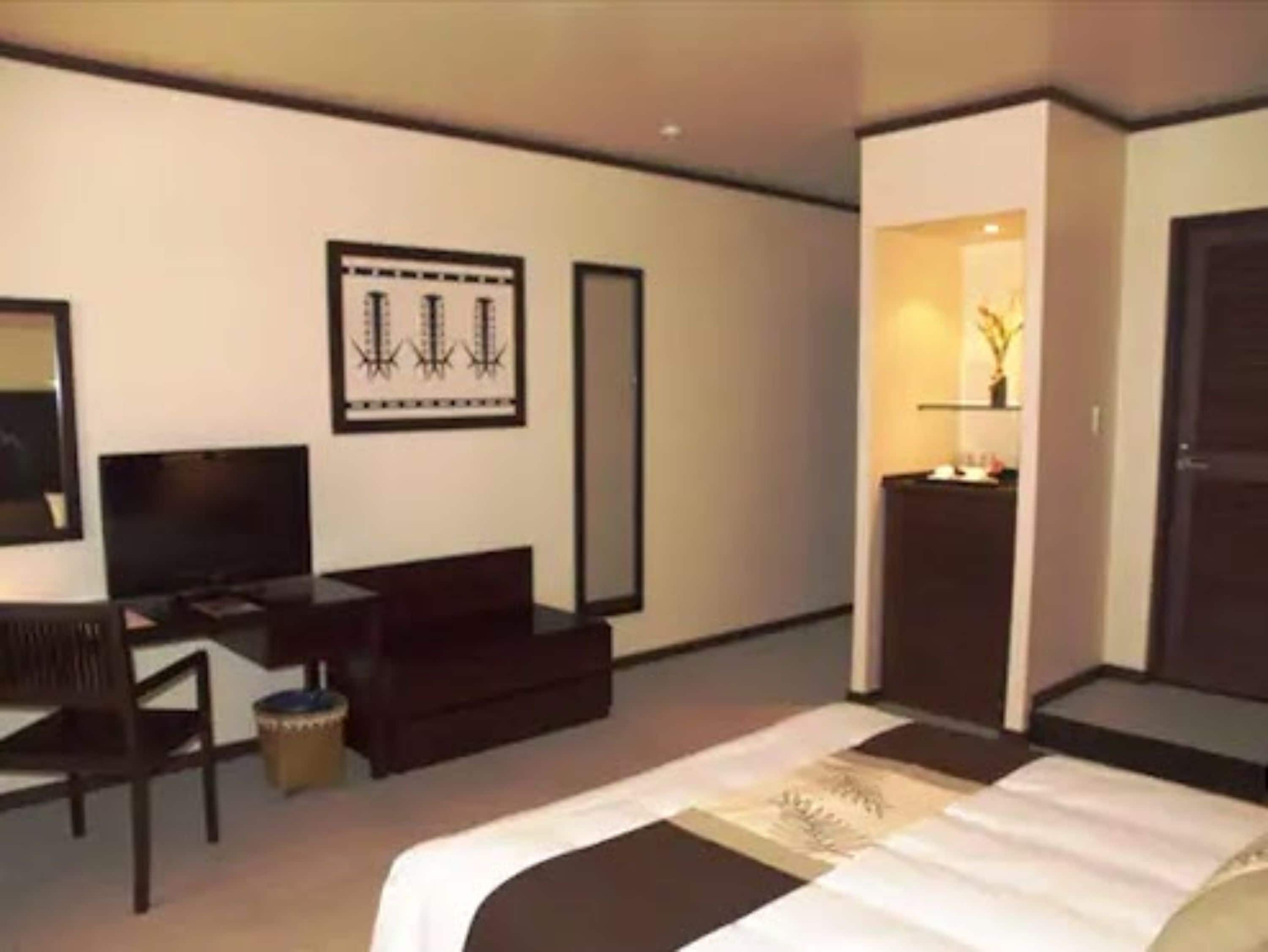 Quarto de hotel moderno com uma cama, uma escrivaninha, uma cadeira, uma TV e um quadro na parede.