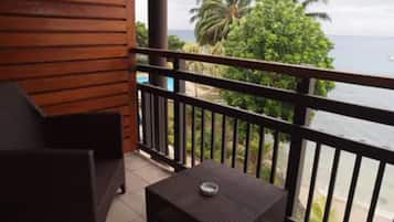 Enjoy the ocean view from this balcony with a table and chair, surrounded by lush greenery.