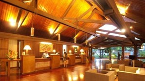 Un vestíbulo amplio con mostradores de recepción de madera, asientos cómodos y un techo alto con vigas a la vista.