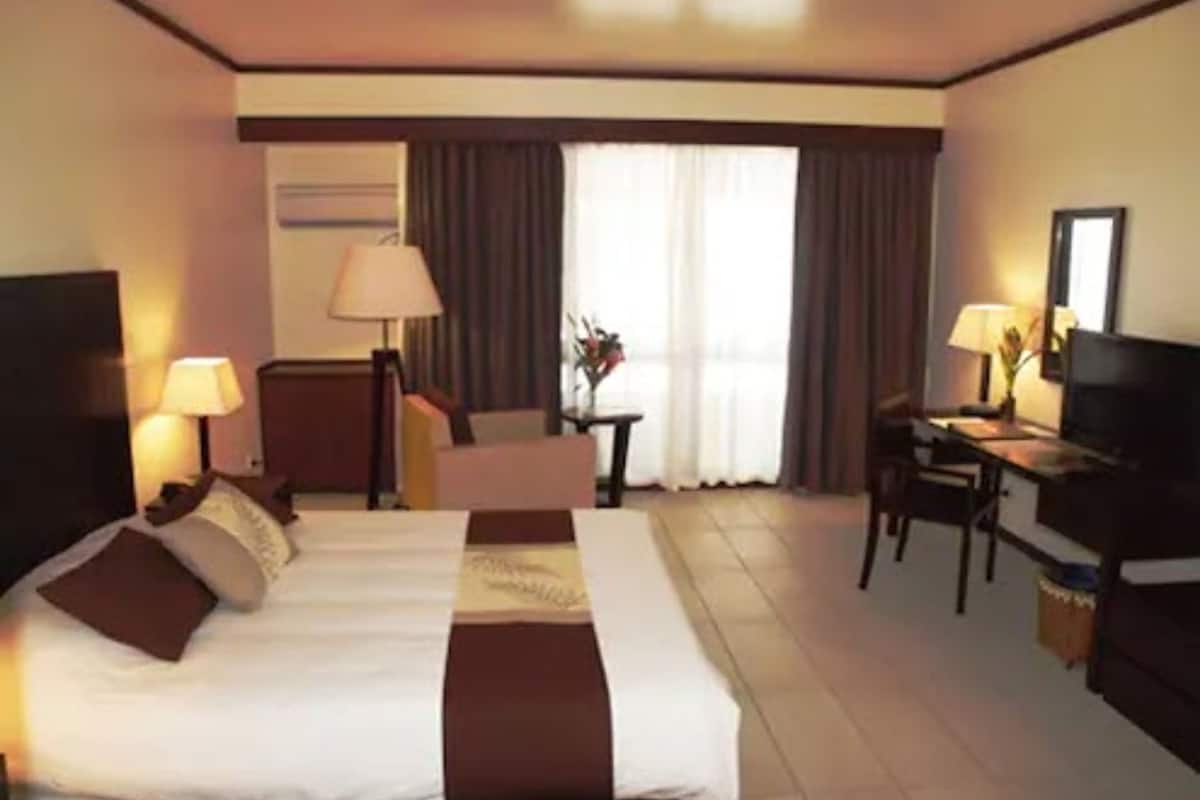 A hotel room with a bed, a desk, a chair, a TV, and a lamp.