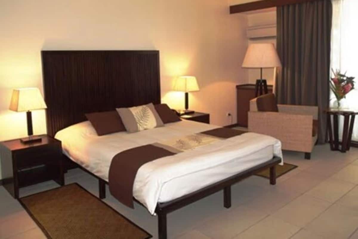 A hotel room with a large bed, two bedside tables with lamps, a chair, and a small table with a vase of flowers.