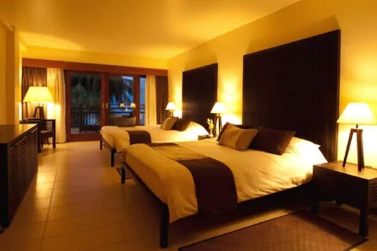 A hotel room with two beds, a desk, and a view of the outdoors.