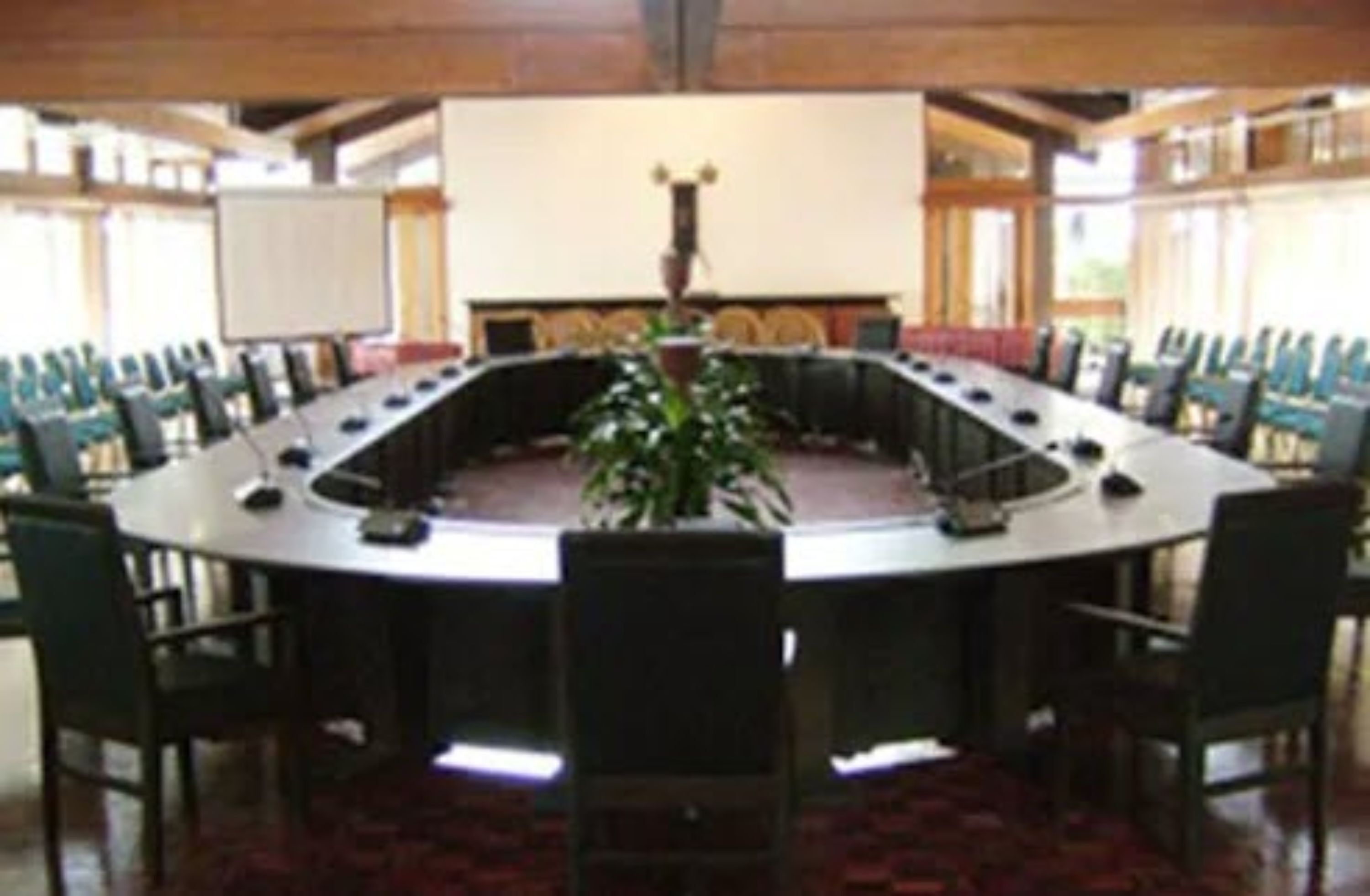 A conference room with a round table, chairs, a whiteboard, and a plant.
