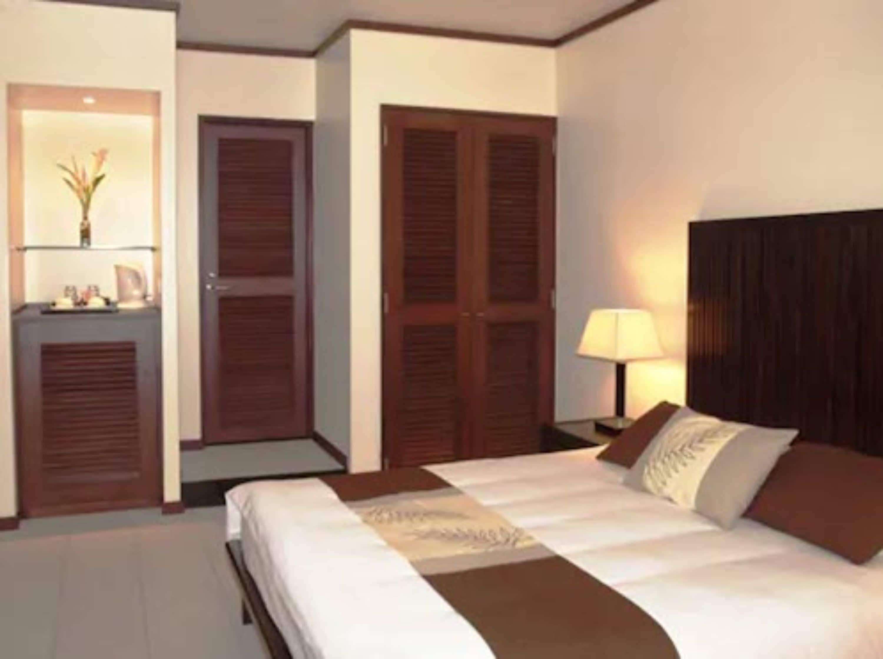 Una habitación de hotel con cama, mesita de noche con lámpara y armario.