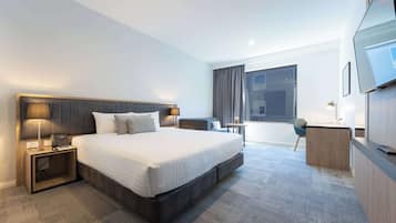 A modern hotel room with a large bed, bedside tables, a desk, and a TV.