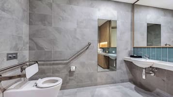 Un baño moderno con inodoro, barra de apoyo, lavabo y espejo.