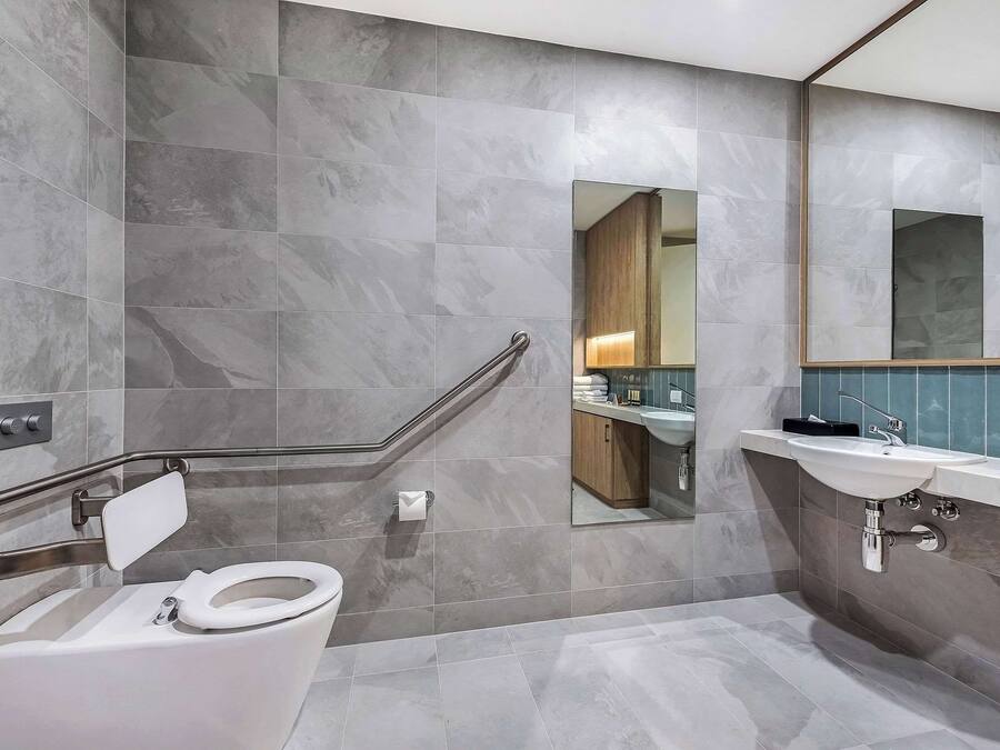 Un baño moderno con inodoro, barra de apoyo, lavabo y espejo.