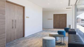 Un vestíbulo moderno con un armario de madera con la etiqueta “EUCA”, un mueble de madera grande con la etiqueta “NORSEMANN” y una zona de estar con otomanas y un sofá.