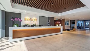 Un área de recepción de hotel moderna con techo de madera, mostrador de recepción y un amplio ventanal con vistas al exterior.
