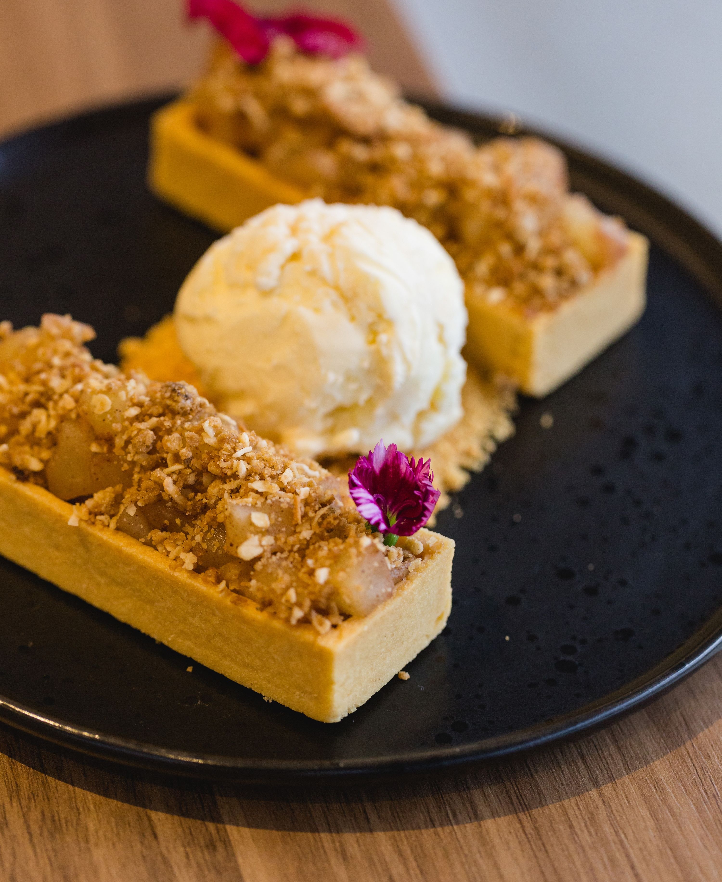 Un plato de postre con un pastelito cubierto de cobertura desmenuzada y una bola de helado.