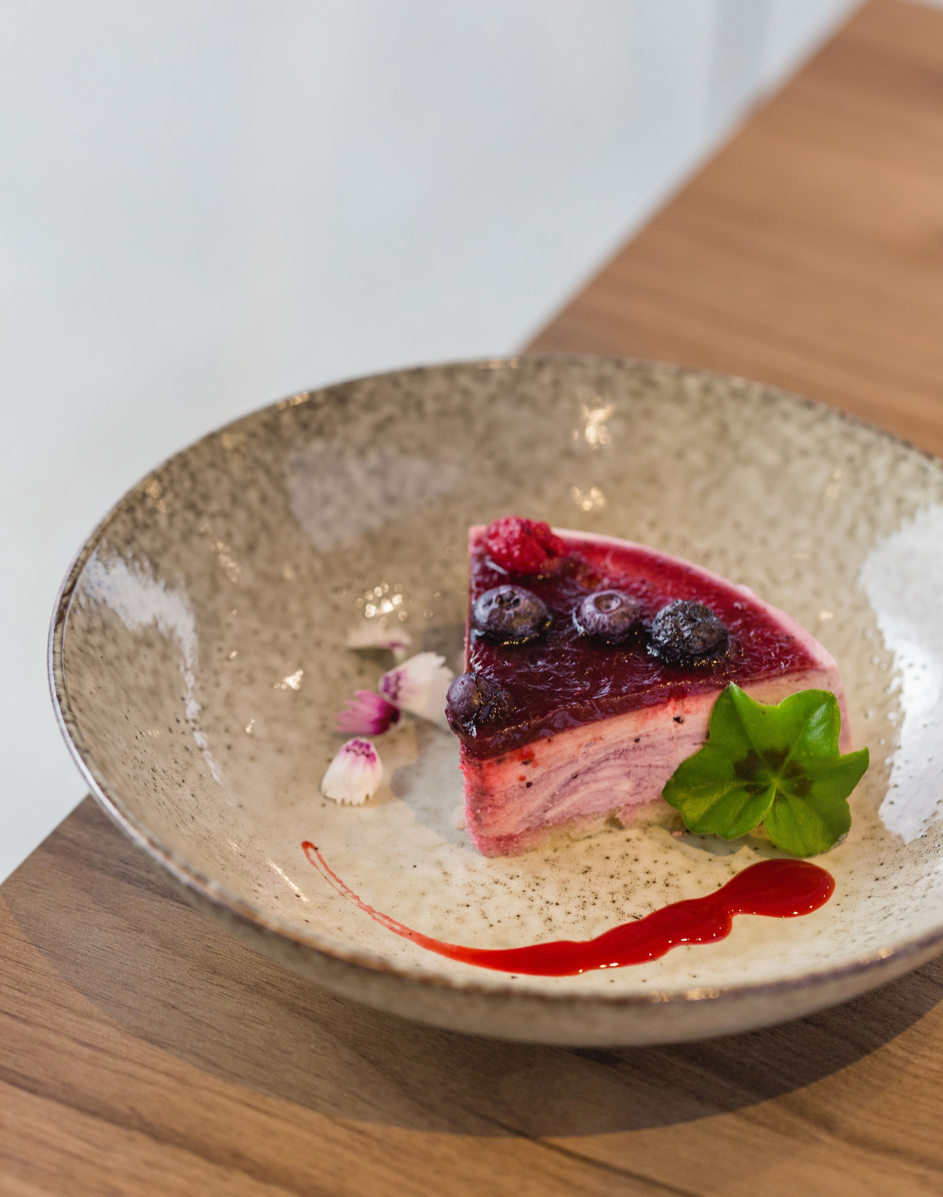 A slice of pie with berries and a mint leaf on a ceramic plate.