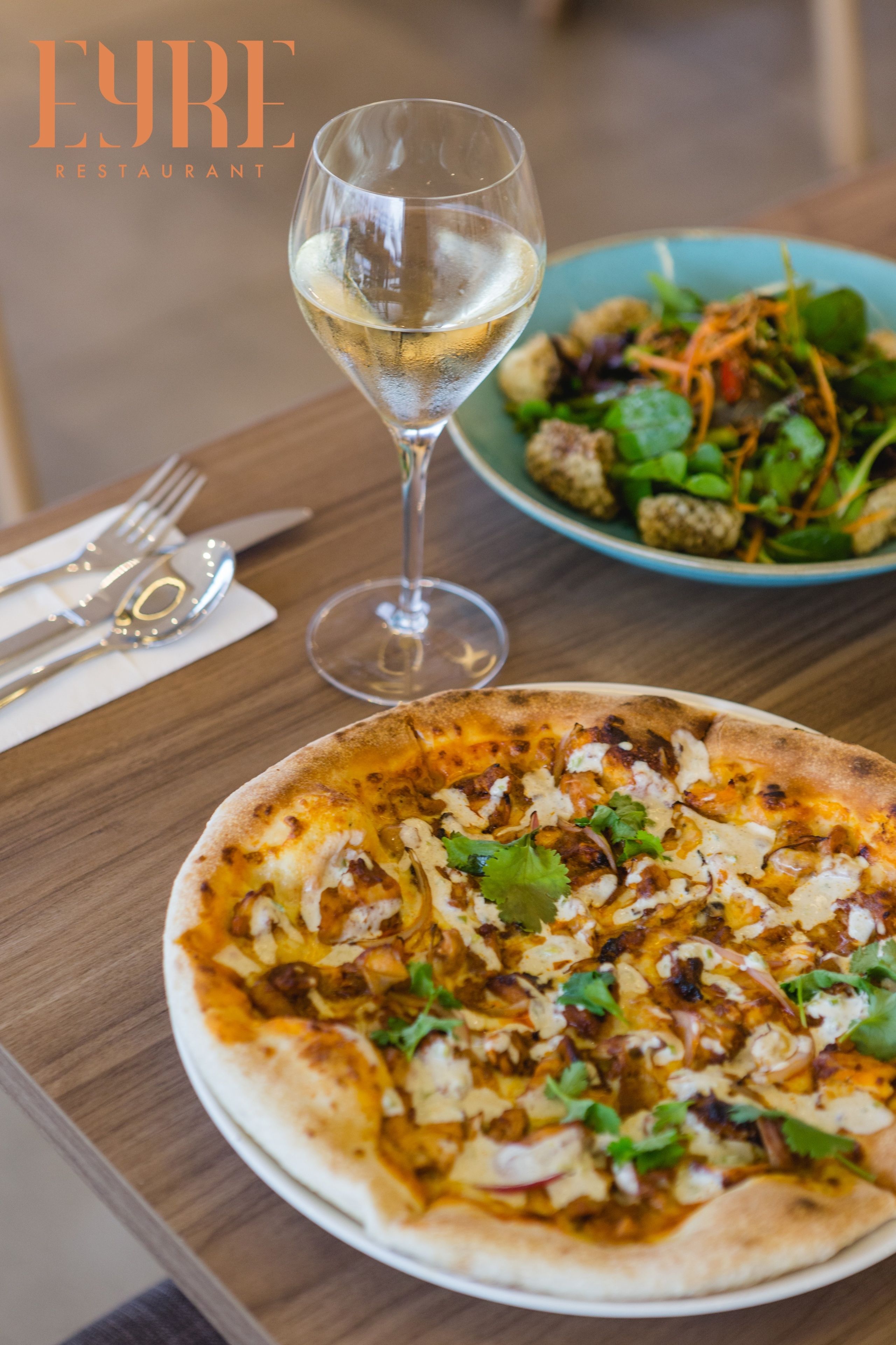 A pizza with toppings and a glass of white wine on a wooden table.