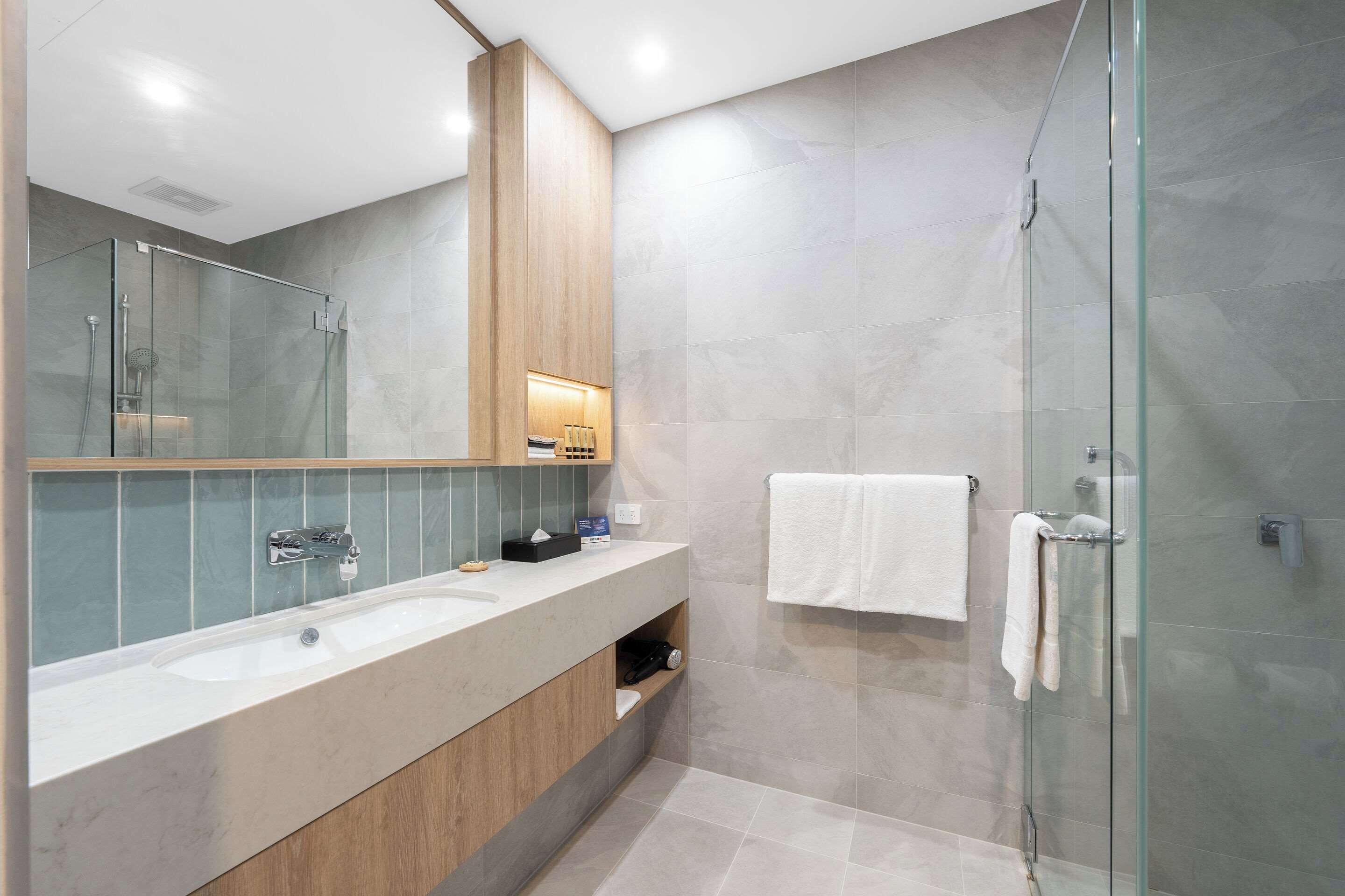 A modern bathroom with a glass shower enclosure, a large mirror, and a vanity with a sink and towel rack.